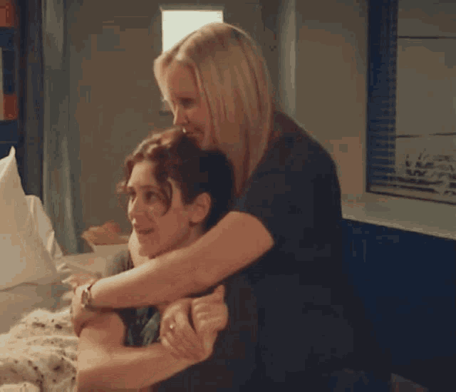two women are hugging each other while sitting on a bed .