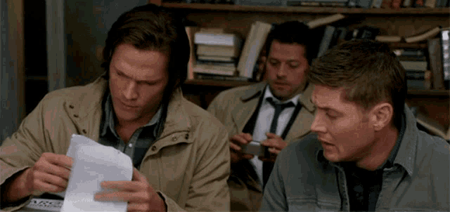 three men are sitting at a table looking at a piece of paper with a calculator on it