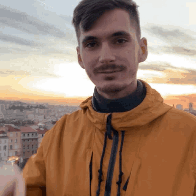 a man in a yellow jacket stands in front of a city skyline at sunset