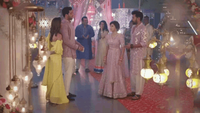 a group of people are standing in a room with a red carpet and lamps .