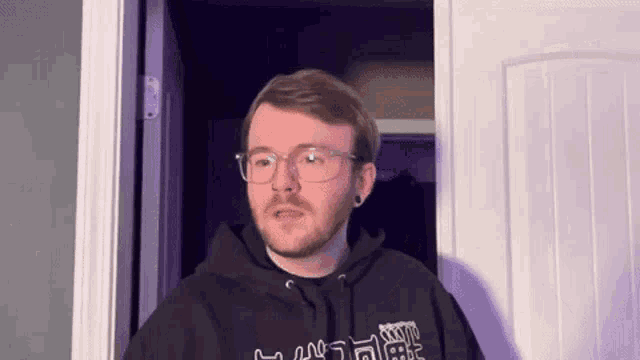 a man with glasses and a beard is standing in front of a door .