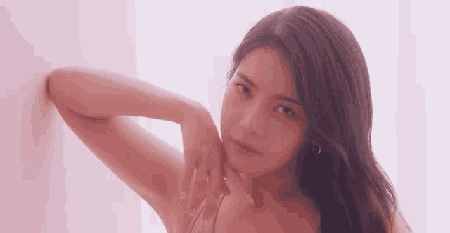 a woman with long dark hair is leaning against a pink wall