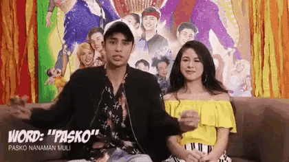 a man and a woman are sitting next to each other on a couch in front of a poster .