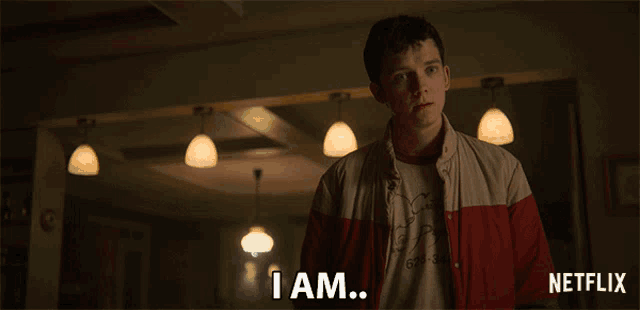a man in a red and white jacket says " i am " in a dark room