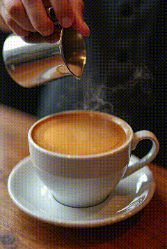 a person is pouring milk into a cup of cappuccino