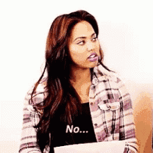 a woman in a plaid shirt is holding a piece of paper with the word no on it .