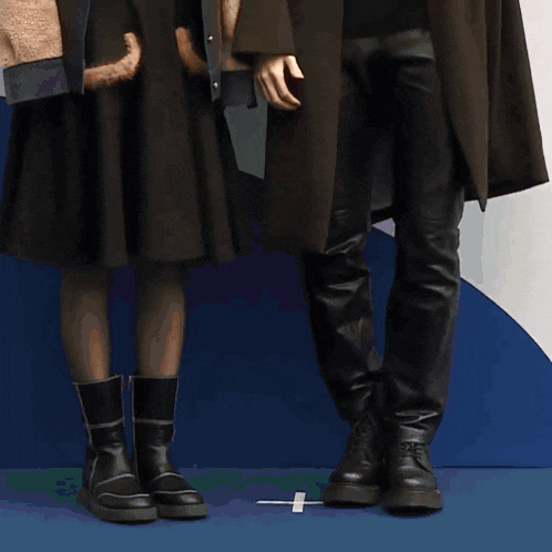 a woman wearing a leopard print jacket and a black skirt stands next to a man wearing a black coat