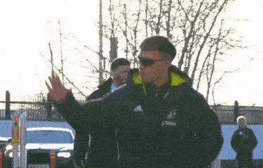 a man wearing sunglasses and an adidas jacket waves