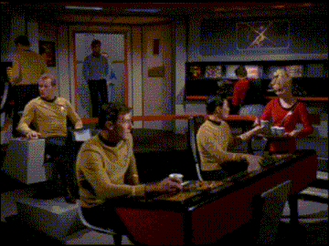 a group of people are sitting at a table in a room with a woman serving them food