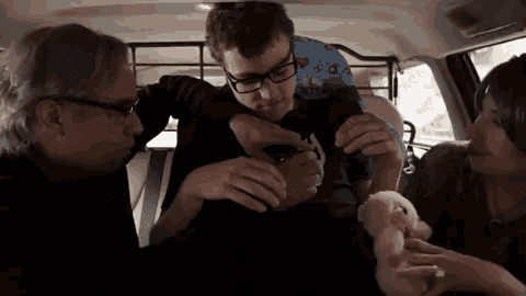 a man wearing glasses is holding a child in a car while a woman holds a stuffed animal