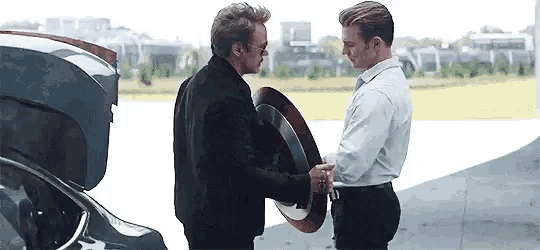 two men are shaking hands while holding a shield in front of a car .