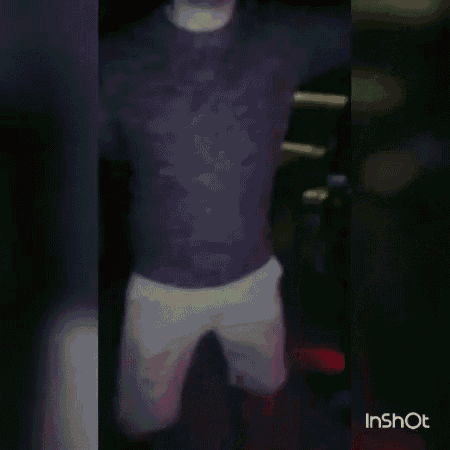 a man in a red shirt is dancing in a dark room with a red light behind him .