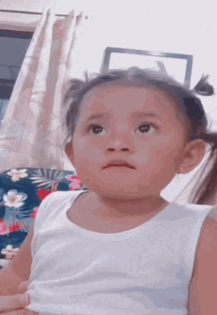 a little girl is wearing a white tank top and looking up