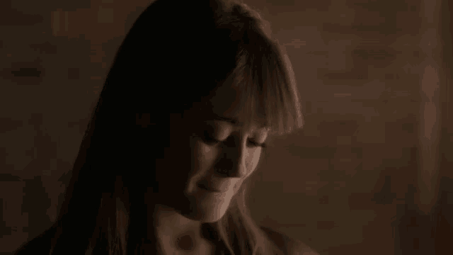 a close up of a woman 's face in the dark with a brick wall in the background .