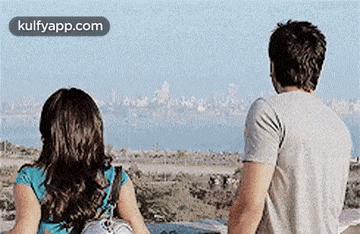 a man and a woman are standing next to each other looking at the ocean .