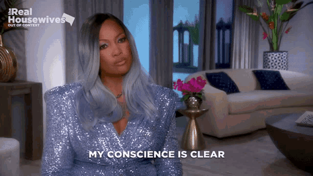 a woman in a blue sequined dress is sitting in a living room and says " my conscience is clear "