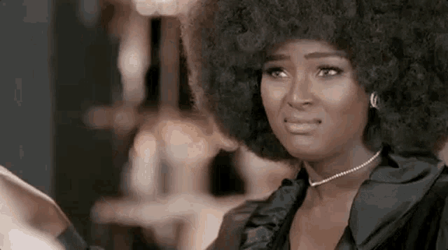 a woman with an afro and a pearl necklace is making a face .