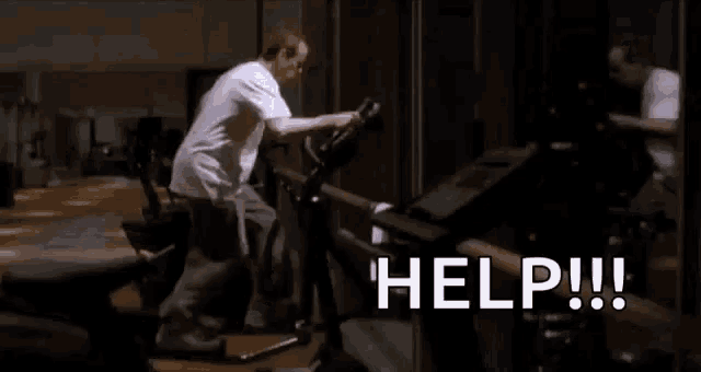 a man is riding an exercise bike in a gym with the words `` help '' written on the screen .