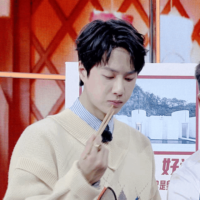 a man wearing a sweater and a striped shirt is eating with chopsticks