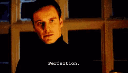 a man in a black turtleneck is standing in front of a window with perfection written on the bottom of his face .