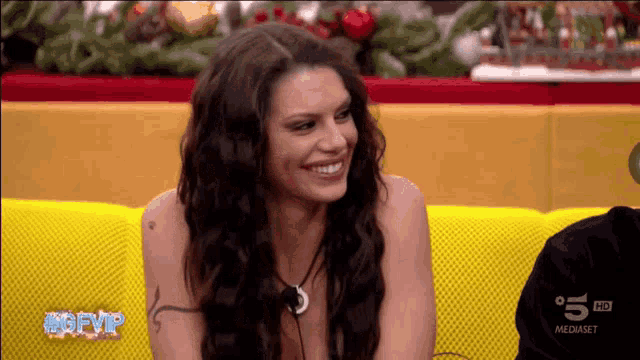 a woman is smiling while sitting on a yellow couch with the words #gfvip on the bottom