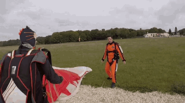 a man in an orange suit is standing in a field holding a red and white parachute