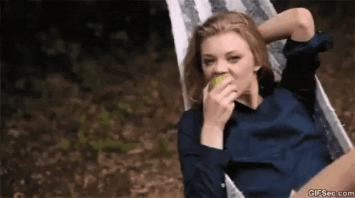 a woman is sitting in a hammock eating a green apple .