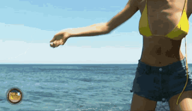 a woman in a yellow bikini and shorts is standing in the water with a logo that says isola paradiso