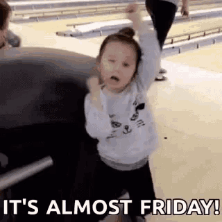 a little girl is dancing in a bowling alley with her arms in the air .