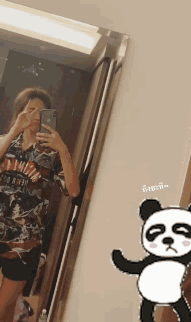 a woman is taking a selfie in front of a mirror with a panda in the corner