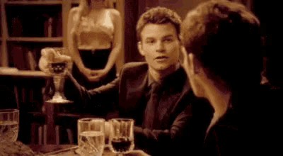 a man in a suit and tie is holding a glass of wine while sitting at a table with a woman .