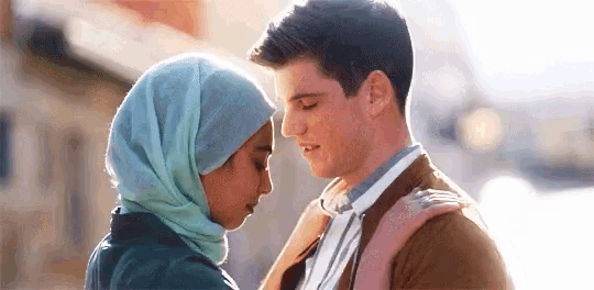 a man and a woman are looking into each other 's eyes . the man is wearing a hijab .