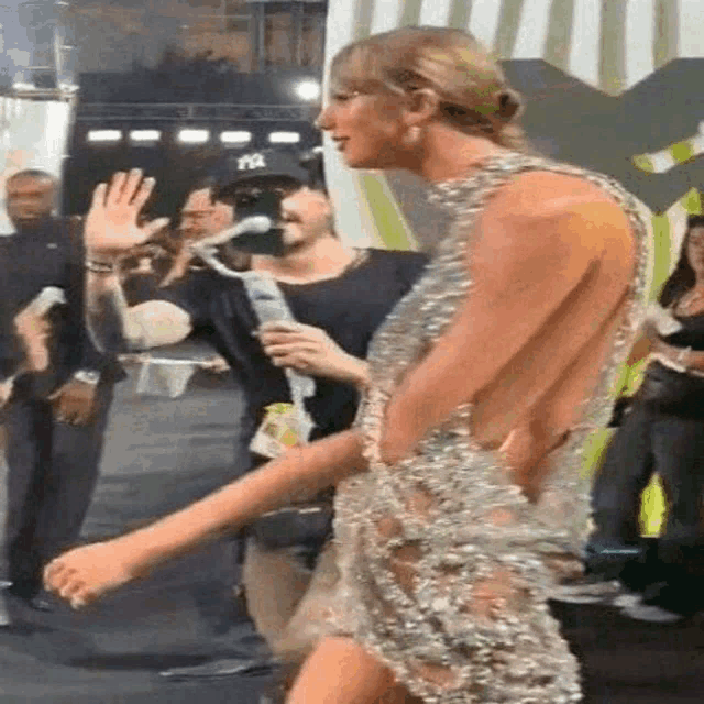 a woman in a very revealing dress is walking down a red carpet while a man holds a microphone .