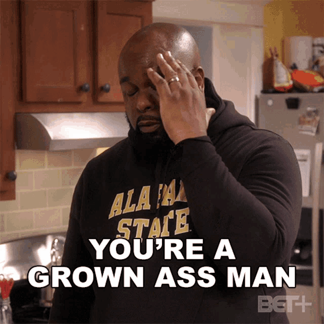 a man wearing an alabama state shirt says you 're a grown ass man in a kitchen