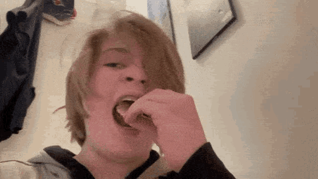 a young man with long hair is eating a piece of food