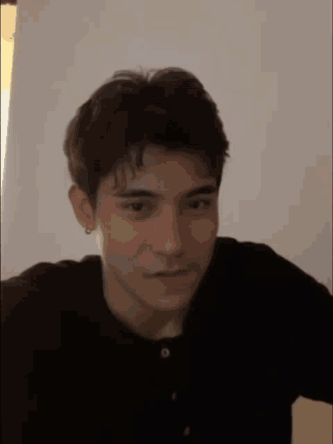 a young man wearing a black shirt and earring looks at the camera