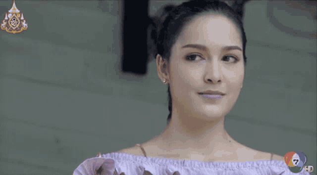 a woman in a purple off the shoulder top is smiling and looking at the camera .