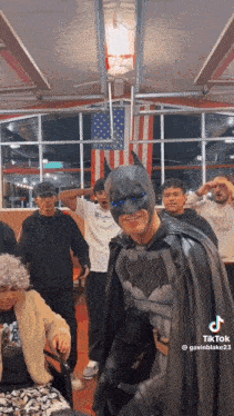 a man in a batman costume is standing in a room with other people .