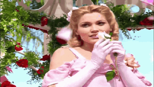 a woman in a pink dress and gloves holds a rose