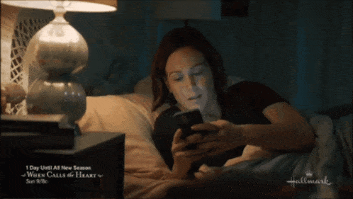 a woman laying on a bed looking at her phone with the words well i guess i 'm up