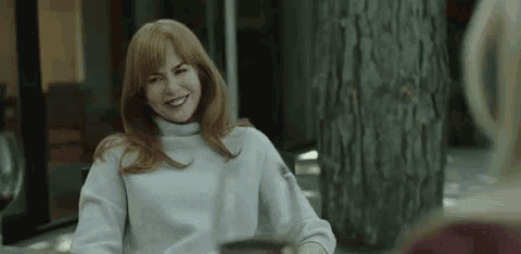 a woman is sitting at a table with a cup of coffee and smiling at the camera .