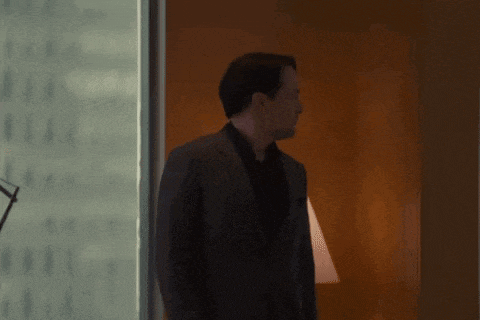 a man in a suit and black shirt is standing in a room .
