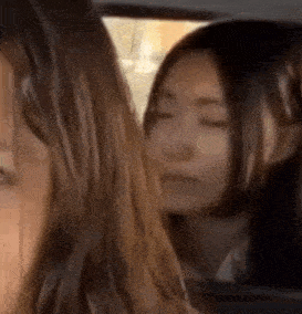 two women are sitting in a car and one of them is looking out the window .
