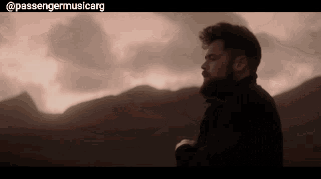 a man with a beard is standing in front of a mountain with the words " passengermusicarg " on the bottom