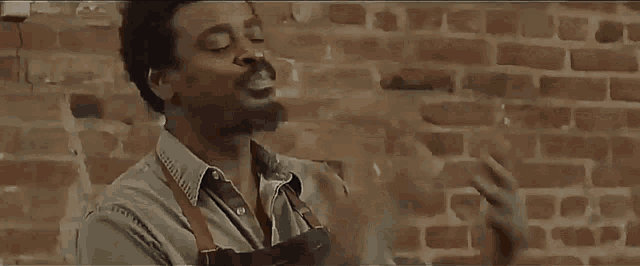 a man is standing in front of a brick wall smoking a cigarette .