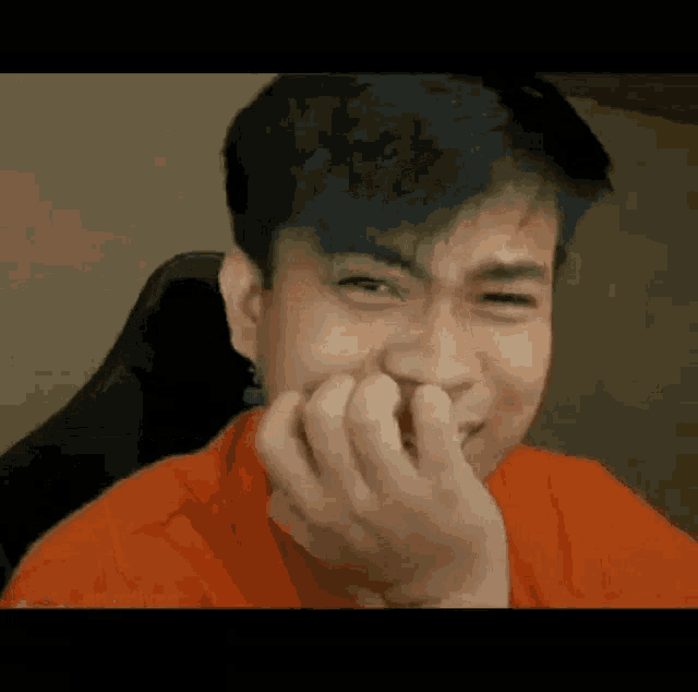 a man in an orange shirt is laughing with his hand on his mouth .