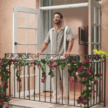 a man standing on a balcony with flowers hanging from the railing
