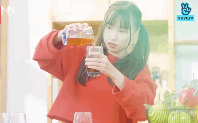 a woman in a red sweater is pouring a drink into a glass with a straw .