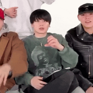 a group of young men are sitting next to each other and one of them is wearing a green sweater .