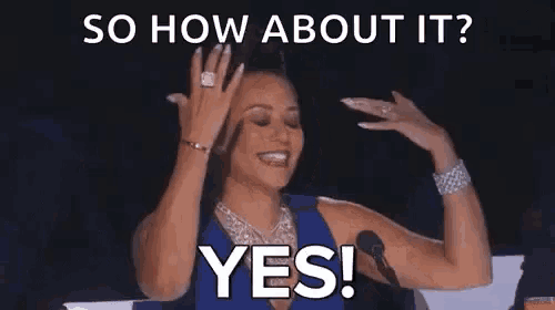 a woman is sitting in front of a microphone with her hands in the air and says `` so how about it ? yes ! ''